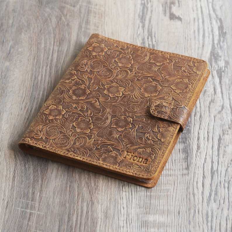 May include: A brown leather journal with a floral embossed design and the name "Fiona" embossed on the front.