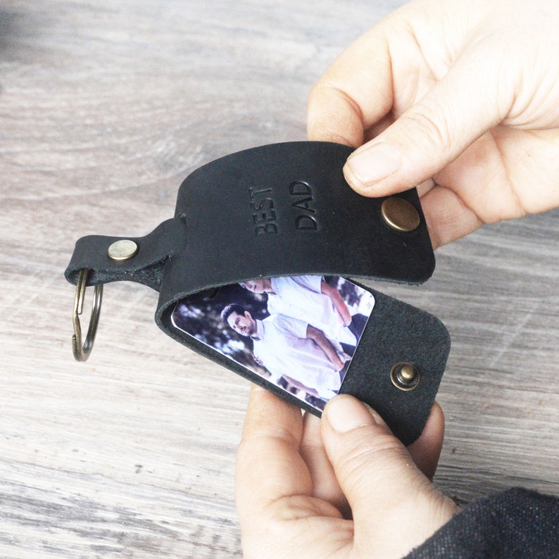 May include: Black leather keychain with a photo insert and a metal ring. The keychain has the words "Best Dad" embossed on the front.