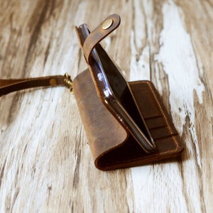 Peut inclure: Un &eacute;tui de t&eacute;l&eacute;phone en cuir marron avec un rabat qui se replie sur l'&eacute;cran. L'&eacute;tui est dot&eacute; d'une sangle et de plusieurs fentes pour cartes.
