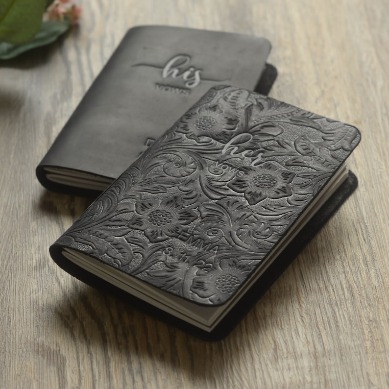 May include: Two black leather journals with embossed floral designs. One journal has the text "his vows" on the cover, and the other has the text "her vows".
