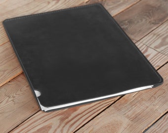 May include: A black leather notebook with a white edge on a wooden surface.