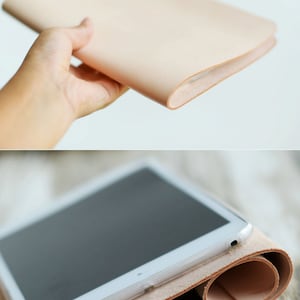 May include: A light brown leather tablet case with a white tablet inside. The case is rolled up and the tablet is visible on the top of the roll.