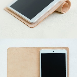 May include: A light brown leather case for a tablet. The case is folded in half and the tablet is inside. The tablet has a black screen and a white frame.