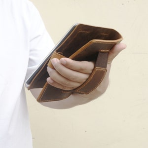 Peut inclure: Une housse de tablette en cuir marron avec une sangle pour le transport. La housse est ouverte et l'int&eacute;rieur est visible.