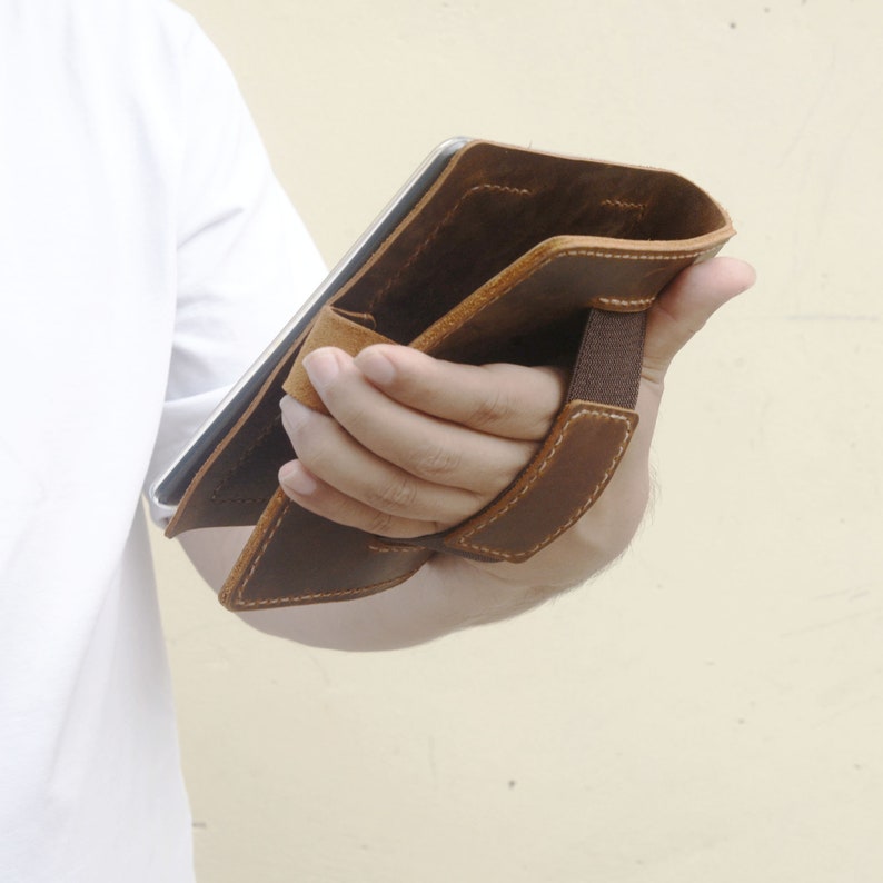 Peut inclure: Une housse de tablette en cuir marron avec une sangle pour le transport. La housse est ouverte et l'int&eacute;rieur est visible.