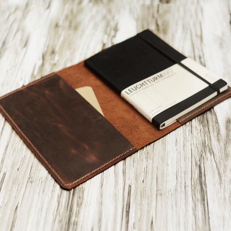May include: A brown leather notebook cover with a black notebook inside. The notebook has the text "LEUCHTTURM1917" on the cover.