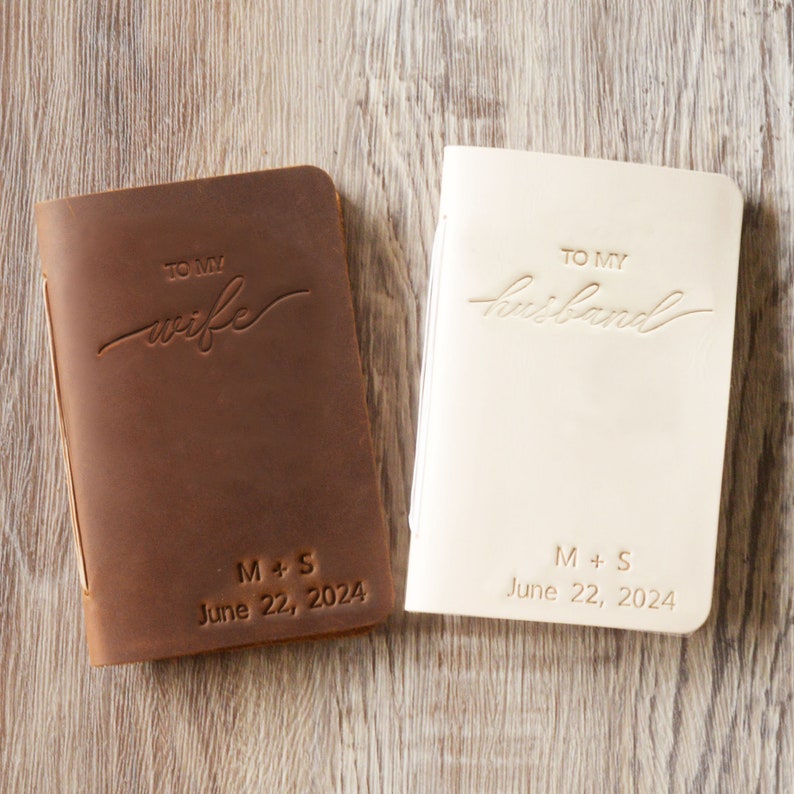 May include: Two leather-bound journals with personalized inscriptions. The brown journal says "To My Wife" and the cream journal says "To My Husband". Both journals have the initials "M+S" and the date "June 22, 2024" embossed on the front.