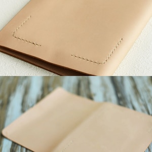 May include: A light brown leather notebook cover with stitching around the edges. The cover is folded in half and has two holes punched in the front.