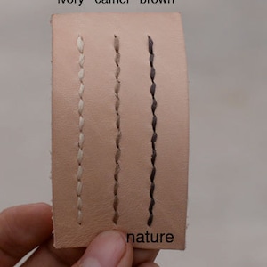 May include: A close-up of a leather swatch with three different colored stitching. The stitching is labeled "ivory", "camel", and "brown". The swatch is labeled "nature".