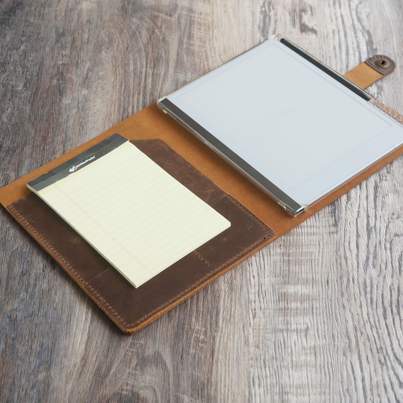 May include: A brown leather portfolio with a clear plastic writing surface and a notepad inside. The portfolio has a flap with a snap closure and a metal clip.