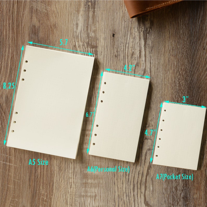 May include: Three different sizes of blank, off-white, paper notebook refills. The refills are punched with six holes on the left side. The sizes are labeled A5 (8.25 inches by 5.7 inches), A6 (6.7 inches by 4.2 inches), and A7 (4.7 inches by 3 inches).