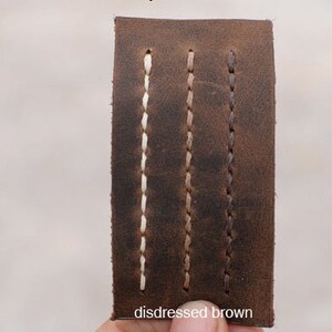 May include: Close-up of a leather swatch showing three different stitching colors: ivory, camel, and brown. The leather is distressed brown.
