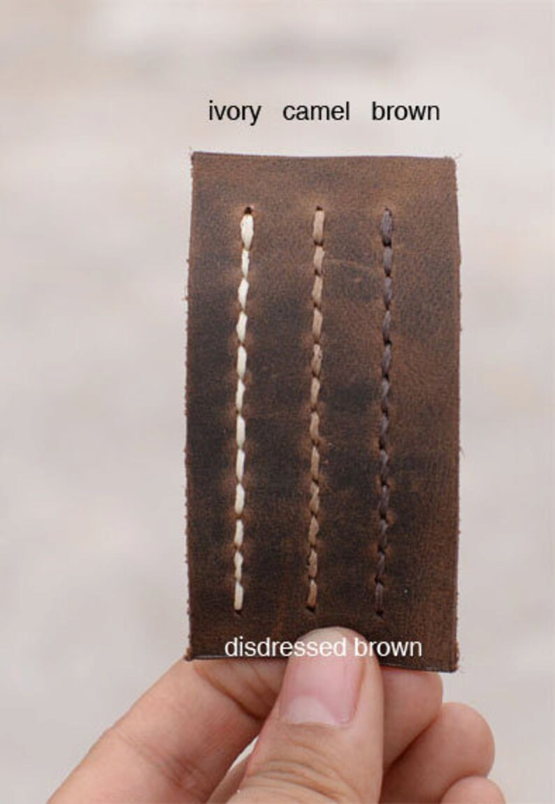 May include: Close-up of a leather swatch showing three different stitching colors: ivory, camel, and brown. The leather is distressed brown.