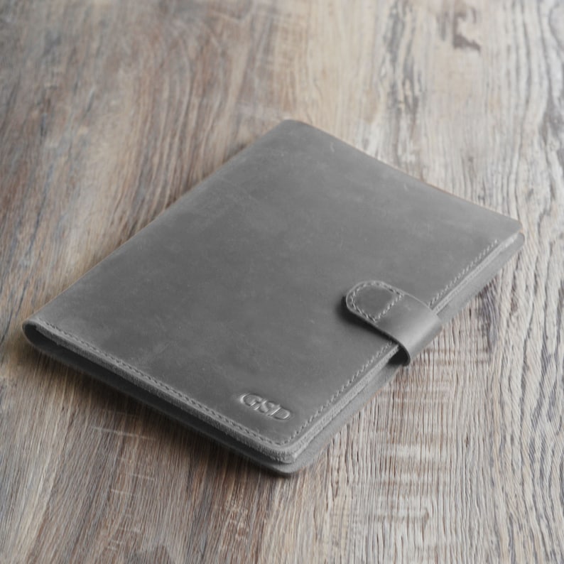 May include: A grey leather folder with a flap closure and a personalised monogram "GSD" embossed on the front.