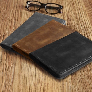 Puede incluir: Tres cubiertas de cuero en diferentes colores: negro, marr&oacute;n y gris. Las cubiertas est&aacute;n apiladas una encima de la otra sobre una superficie de madera.