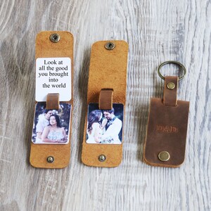 May include: A brown leather keychain with a photo insert and a message that reads "Look at all the good you brought into the world". The keychain also has a separate leather tag that says "DAD".