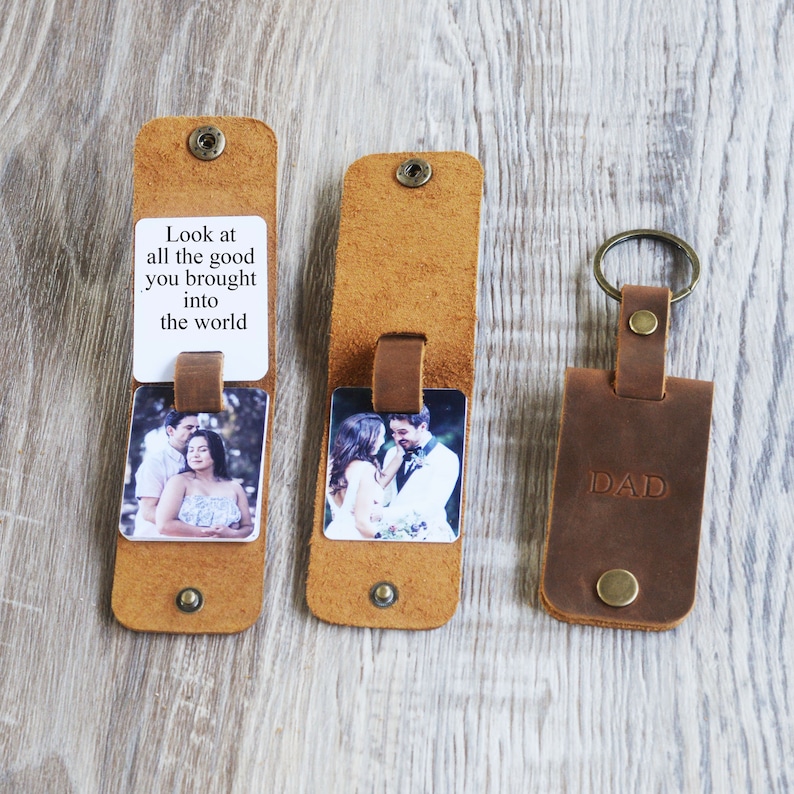 May include: A brown leather keychain with a photo insert and a message that reads "Look at all the good you brought into the world". The keychain also has a separate leather tag that says "DAD".