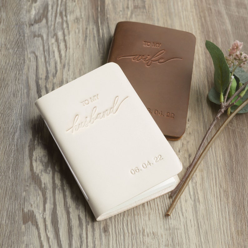 May include: Two small leather-bound journals with embossed text. One is white with the text "To my husband 06.04.22" and the other is brown with the text "To my wife 13.04.22".