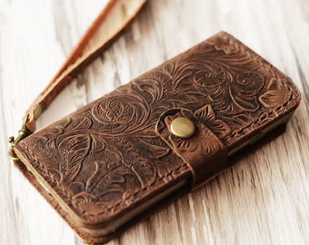 Peut inclure: Une coque de téléphone en cuir marron avec un motif en relief floral et une sangle. La coque a une fermeture à bouton en laiton.
