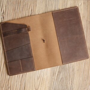 May include: A brown leather notebook cover with multiple pockets and a flap closure. The cover is open to reveal a tan interior.