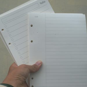 May include: Two white, blank, lined paper pads with holes for a binder. The top pad has the word "To Do" written on it. The bottom pad has the word "CUE" written on it.