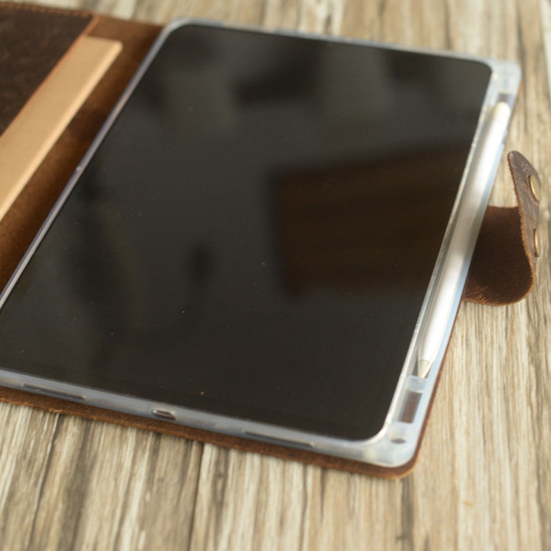 May include: A brown leather case with a flap that folds over to protect a tablet and stylus. The tablet is black and the stylus is white.