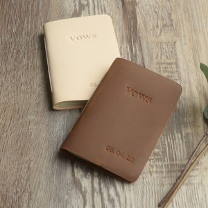 May include: Two leather-bound vow books, one brown and one cream, with the word "Vows" embossed on the front. The brown book has the date "05.04.22" embossed on the front.