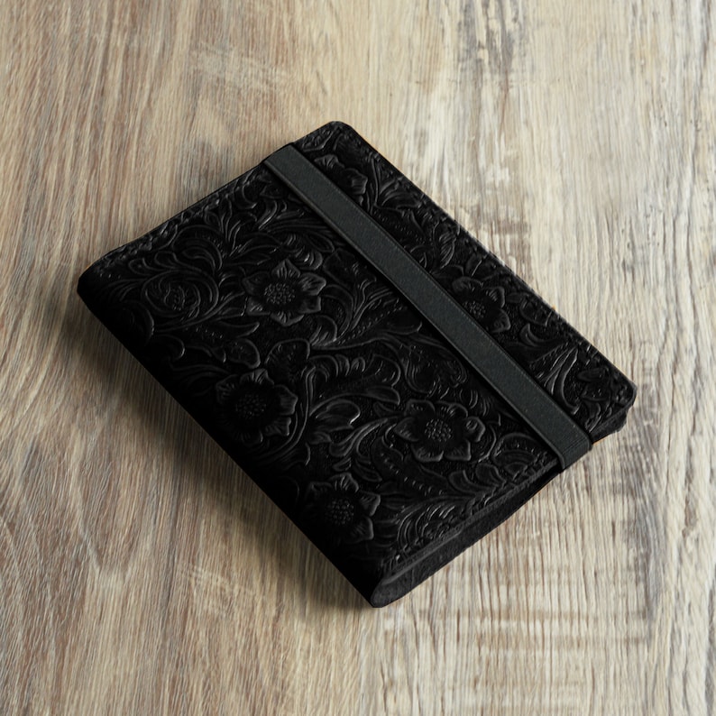 Peut inclure: Un portefeuille en cuir noir avec un motif floral en relief et une fermeture &agrave; bande &eacute;lastique noire.