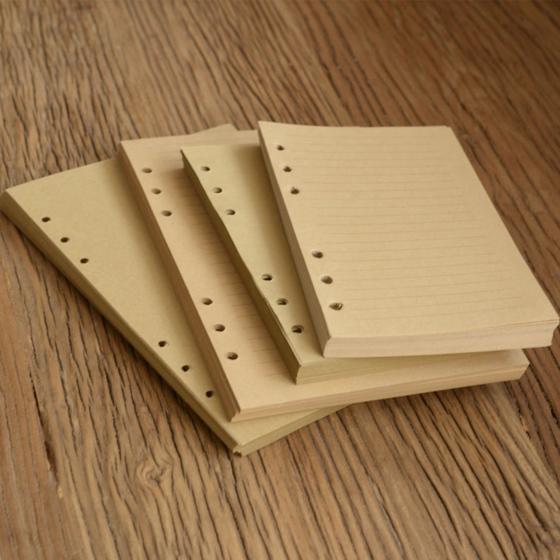 May include: Four brown paper notebooks with punched holes along the spine. The notebooks are stacked on top of each other and have lined paper.