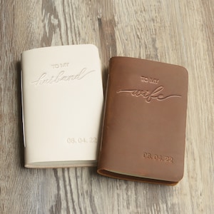 May include: Two leather-bound journals, one white and one brown, with the words "To My Husband" and "To My Wife" embossed on the covers. The date "06.04.22" is also embossed on each journal.