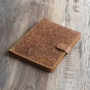 May include: A brown leather journal with a floral embossed design and a clasp closure. The journal has the word "Tone" embossed on the front cover.