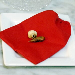 May include: A red fabric pouch with a white drawstring, sitting on a white plate. Inside the pouch are two small, brown, dried objects.