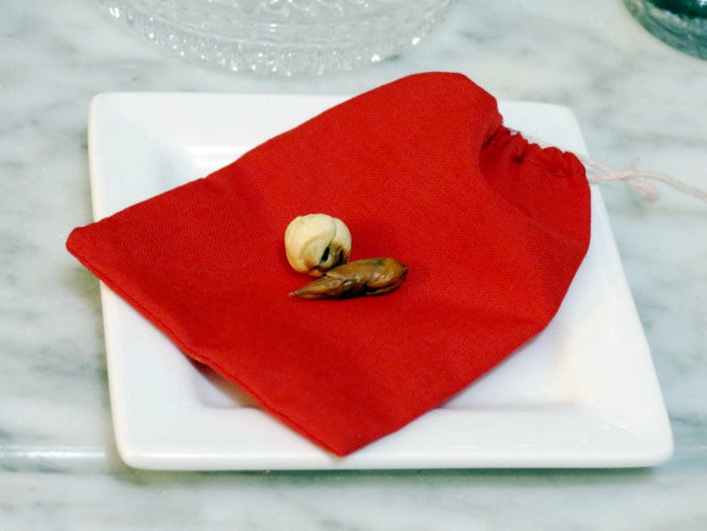 May include: A red fabric pouch with a white drawstring, sitting on a white plate. Inside the pouch are two small, brown, dried objects.