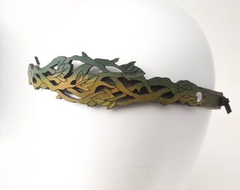 May include: A leather headband featuring a laser-cut vine and leaf pattern with a gradient color transition from dark green to yellow. The accessory is secured with a silver-toned metal rivet on the side and has a thin black cord tie closure.