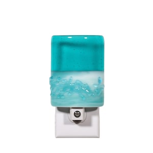 May include: A rectangular glass night light featuring a solid teal top section and a white bottom section with a textured, raised light blue wave-like pattern across the middle. The glass is mounted on a standard white plastic wall plug base.