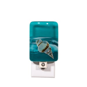 May include: A rectangular fused glass night light featuring a deep teal and turquoise background with a white wave pattern and a central light blue seashell motif with brown textured accents, mounted on a standard white electrical plug base.