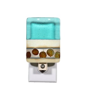 May include: A rectangular glass night light featuring a translucent turquoise top section with small air bubbles, a solid white middle band, and a bottom section decorated with a horizontal row of six circular amber-colored glass accents.