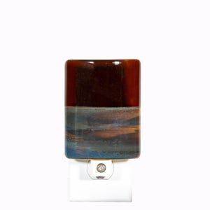 May include: A rectangular night light featuring a glossy ceramic cover with a two-tone design. The top half is a solid deep brown, while the bottom half displays a blended pattern of blue, gray, and brown tones. It is attached to a white plug-in base.