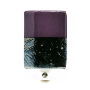 May include: A rectangular glass night light with a purple top and a black and gray bottom. The night light has a white plug and a green light.
