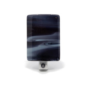 May include: A black and white glass night light with a swirling pattern. The light is plugged in and turned on, illuminating the room with a soft glow.