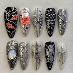 May include: A set of ten press-on nails featuring intricate 3D designs. The collection includes black and white bases adorned with silver metallic filigree, raised floral motifs in pink, a central opal-like stone, a unicorn illustration, and a sword.