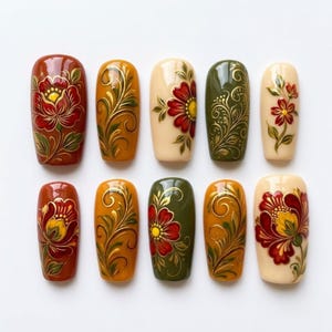 May include: A set of ten press-on nails featuring intricate hand-painted floral designs and golden filigree swirls. The colour palette includes deep red, mustard yellow, olive green, and cream, with glossy finishes on each rectangular nail tip.