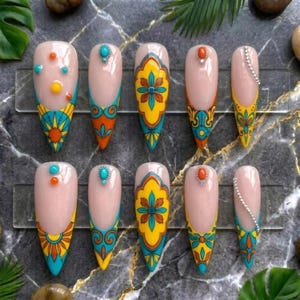 May include: A set of ten artificial nails with a light pink base, featuring intricate designs in turquoise, yellow, orange, and white. Some nails have small gemstone accents or a chain of rhinestones. The designs showcase floral and geometric patterns.