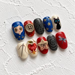 May include: A set of ten press-on nails featuring detailed hand-painted designs including a blue-haired character with button eyes, a large button, a spider web, gold stars on blue, a black cat, a needle and thread, a flower, a star, a spiral, and a dragonfly.