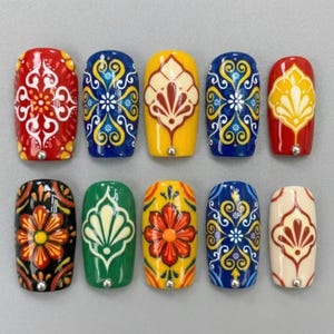 May include: A set of ten press-on nails with intricate, colorful designs. Each nail features a different pattern, including floral and geometric motifs, in shades of red, blue, yellow, green, black, and cream. The nails have a glossy finish and a small silver bead at the base.