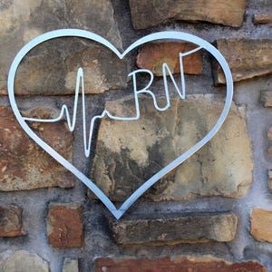 May include: A silver metal heart-shaped sign with a stylised EKG line and the letters "RN" inside. The sign is mounted on a stone wall.