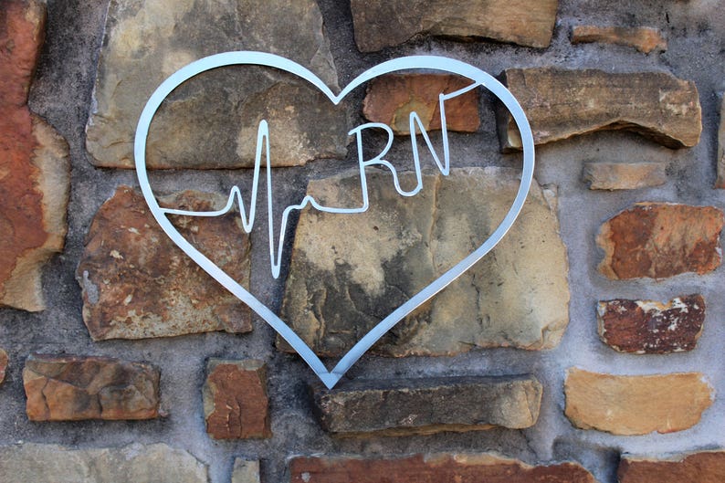May include: A silver metal heart-shaped sign with a stylised EKG line and the letters "RN" inside. The sign is mounted on a stone wall.