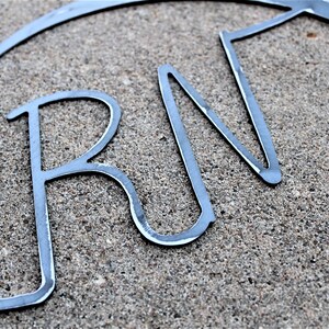 May include: Metal wall decor in the shape of a heart with the letters "RN" inside. The letters are made of thin metal and are slightly curved.