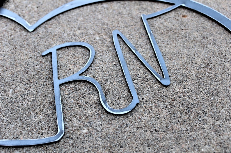 May include: Metal wall decor in the shape of a heart with the letters "RN" inside. The letters are made of thin metal and are slightly curved.