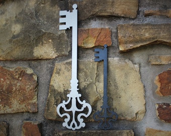 May include: Two decorative metal keys, one silver and one black, are mounted on a stone wall. The keys are ornate and have intricate designs.